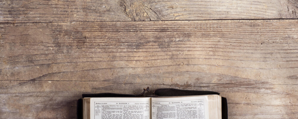 Opened bible on a wooden desk background.